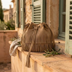 Khaki camel fringe bucket bag styled in a warm Mediterranean setting