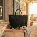 Black canvas fringe tote bag styled in a warm Mediterranean setting