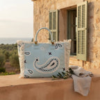 Light Blue canvas fringe tote bag styled in a warm Mediterranean setting