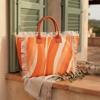Orange canvas fringe tote bag styled in a warm Mediterranean setting
