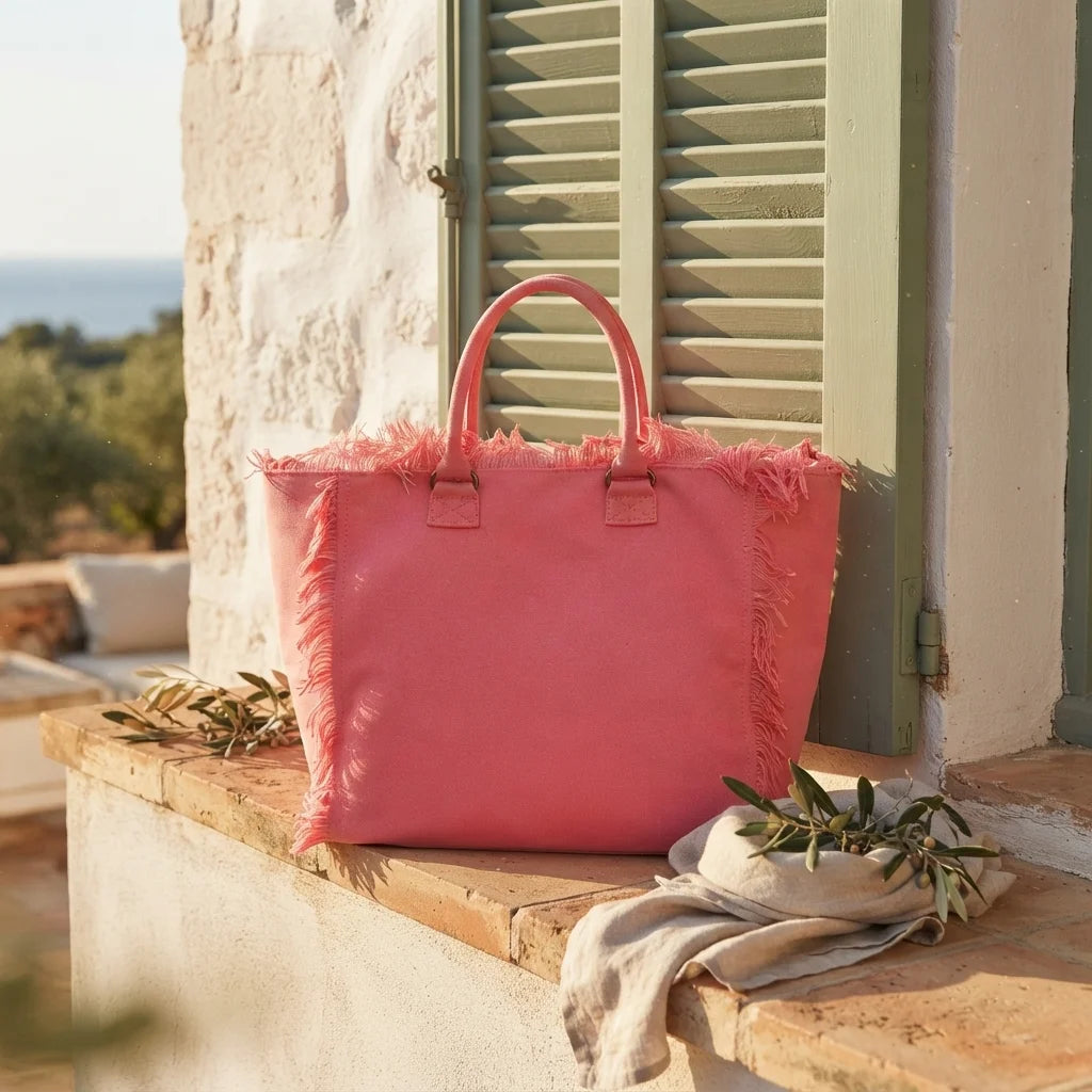 Pink canvas fringe tote bag styled in a warm Mediterranean setting