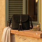 Black cowhide crossbody bag with fringe styled in a warm Mediterranean setting