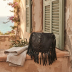 Black designer fringe crossbody bag styled in a warm Mediterranean setting