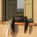 Black fringe clutch crossbody bag styled in a warm Mediterranean setting