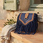 Blue fringed suede sling bag styled in a warm Mediterranean setting