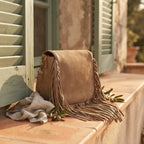 Camel fringed suede sling bag styled in a warm Mediterranean setting