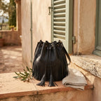 Black leather bucket bag with fringes styled in a warm Mediterranean setting