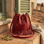 Red leather bucket bag with fringes styled in a warm Mediterranean setting