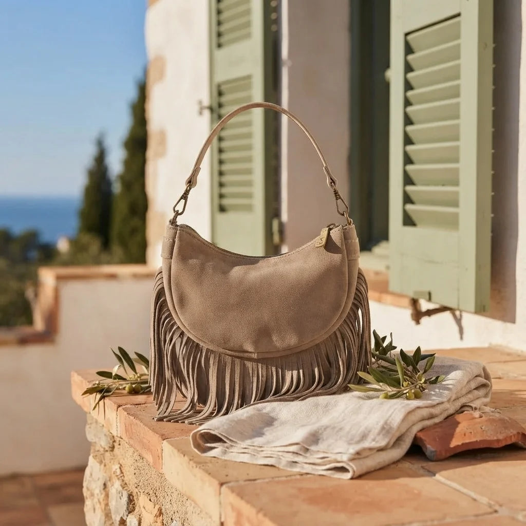 Taupe suede fringe clutch bag styled in a warm Mediterranean setting