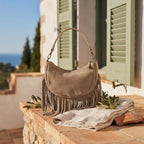 Taupe suede fringe clutch bag styled in a warm Mediterranean setting
